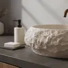A close-up view of a stone-like basin in a bathroom setting, with a soap dispenser and bar of soap visible. Produktbild-Vorschau