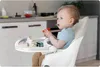 A baby sitting in a high chair in a kitchen. Produktbild-Vorschau