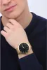 A man wearing a dark blue sweater is showing off a gold watch with a black face on his wrist. Anteprima dell’immagine prodotto
