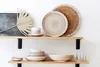 A display of ceramic plates and bowls on two wooden shelves against a white wall. Produktbild-Vorschau