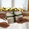 Two people exchanging a gift, with blurred Christmas lights in the background. Podgląd zdjęcia produktu