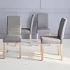 Four gray upholstered dining chairs with light wood legs are arranged in a room with a light gray wall and white floor. Produktbild-Vorschau