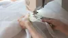 A close-up shot of hands sewing white sheer fabric on a sewing machine. Produktbild-Vorschau