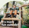 A young boy is happily sitting on a swing set in a wooded area. Podgląd zdjęcia produktu