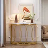 A console table with a marble top and gold metal frame, decorated with a lamp, a framed picture of a flamingo, and a vase with flowers. A sofa is visible in the background. Podgląd zdjęcia produktu