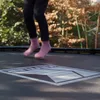 A person's legs and feet are shown jumping on a trampoline outdoors. Podgląd zdjęcia produktu
