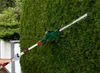 A person is using a telescopic hedge trimmer to trim a tall green hedge. Produktbild-Vorschau