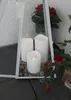 Three LED candles inside a white lantern, surrounded by gravel and red roses. Produktbild-Vorschau