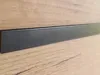 A close-up view of a dark gray metal trim strip against a light brown wood-grain background. Produktbild-Vorschau