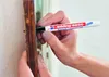 A person's hands are holding a marker and marking a wooden surface. Produktbild-Vorschau