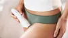 A person is holding a white epilator near their inner thigh. Náhled obrázku produktu