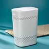 A white laundry basket with a lid and perforated pattern sits on a light beige mat against a blue background. Produktbild-Vorschau