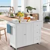 A white kitchen island with a stainless steel countertop is placed in a bright room with a large window overlooking a body of water. The island has two doors, three drawers, and a towel rack with a blue towel. On the countertop, there are plates, a vase of Náhľad obrázku produktu