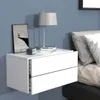 A white floating nightstand with two drawers is mounted on a light blue wall next to a bed with gray pillows. Produktbild-Vorschau
