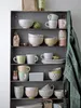 A collection of ceramic mugs and bowls arranged on shelves. Produktbild-Vorschau