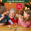 A grandmother and two children are laughing while playing with small wooden games on a table. Produktbild-Vorschau