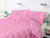 A pink comforter and pillows are neatly arranged on a bed in a bedroom setting. Anteprima dell’immagine prodotto