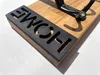 Close-up of a wooden wall hook with the word 'HOME' cut out of a black metal plate. Produktbild-Vorschau