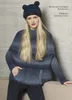 A woman wearing a knitted poncho and hat, posing on a couch. Produktbild-Vorschau