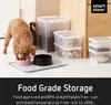 A dog eating from a bowl next to storage containers. Produktbild-Vorschau