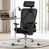 A black ergonomic office chair is shown from the back, positioned in front of a desk with a laptop and a lamp. Produktbild-Vorschau