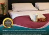 A bed with a burgundy blanket, pillows, a book, and a cup on a tray. Produktbild-Vorschau