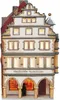 A ceramic miniature house with illuminated windows, depicting a traditional building with arched storefronts. Produktbild-Vorschau
