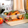 A roasted chicken with vegetables in a glass baking dish on a wooden cutting board. Produktbild-Vorschau