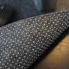A close-up view of a gray desk mat with white polka dots, showing its textured surface and the underside with anti-slip dots. A computer mouse and a metal cup are partially visible in the background. Produktbild-Vorschau