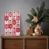 A pink advent calendar with 24 drawers sits on a wooden dresser next to a vase with a Christmas tree branch and gingerbread decorations. Náhled obrázku produktu