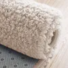 A close-up of a rolled-up beige shaggy rug, showing the texture of the fibers and the non-slip backing. Podgląd zdjęcia produktu