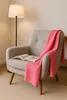 A pink blanket draped over a chair next to a floor lamp. Produktbild-Vorschau