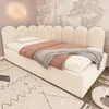 A beige upholstered bed with a scalloped headboard in a child's bedroom. Voir les images du produit