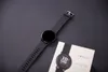 A black smartwatch and its packaging are placed on a dark gray surface. Podgląd zdjęcia produktu