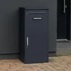 A dark gray parcel mailbox is shown standing next to a dark gray wall and a dark gray door. Náhled obrázku produktu