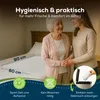 Two women, an older and a younger one, are standing next to a bed with a white underpad on it. The underpad has dimensions indicated. Produktbild-Vorschau