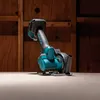 A cordless mini circular saw is shown on a wooden surface, with a wooden wall in the background. Produktbild-Vorschau