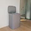 A grey laundry basket with an open lid stands against a white wall in a hallway with wooden flooring. Produktbild-Vorschau