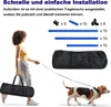 A woman is walking a dog, carrying a black bag. The background shows components of an agility training set. Náhled obrázku produktu