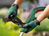 Hands wearing green gloves holding a green and red grass trimmer in an outdoor setting. Anteprima dell’immagine prodotto