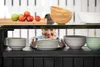 A woman is arranging dishes on a multi-level outdoor kitchen cart. The cart is stocked with various kitchenware and fruit. Náhled obrázku produktu