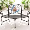 A metal garden bench with a butterfly design on the back, placed outdoors with white flowers in the background. Anteprima dell’immagine prodotto