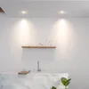 A modern bathroom with a freestanding bathtub, a wooden shelf with towels and toiletries, and recessed ceiling lights. Produktbild-Vorschau