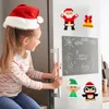A young girl wearing a Santa hat is sitting on the edge of a refrigerator, looking at Christmas-themed magnets on the door. The refrigerator door has a chalkboard with drawings and text. Produktbild-Vorschau