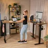 A woman is working at an L-shaped standing desk in a home office setting. Produktbild-Vorschau