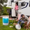A portable washing machine is shown in a garden setting next to a campervan, with people and a dog enjoying a barbecue. Produktbild-Vorschau