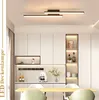 A modern dining room or kitchen area with white cabinets, a wooden table, and chairs, illuminated by a sleek ceiling light. Produktbild-Vorschau