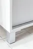 A close-up view of the bottom corner of a white cabinet, showing one of its metal legs. Náhled obrázku produktu