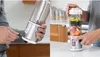 A split image showing a person charging a portable blender on the left and a person pressing a button on a blender filled with ingredients on the right. Podgląd zdjęcia produktu
