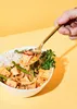 A hand holding a spoon of food over a bowl of rice and curry. Produktbild-Vorschau